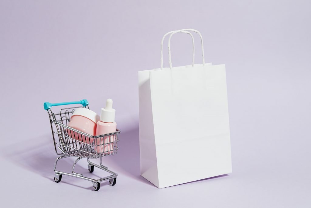 Chariot miniature contenant des produits de beauté et un sac en papier kraft blanc pour illustrer notre guide des meilleurs sites de cosmétiques coréens. 