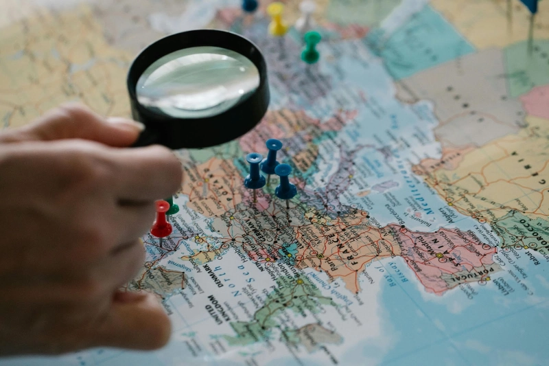 Main tenant une loupe au-dessus d'une carte avec des punaise placées sur certains lieux pour un voyage en Corée du Sud